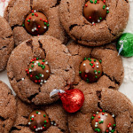 Chocolate peanut butter blossoms on white cookie tray with red and green wrapped hershey's kisses.