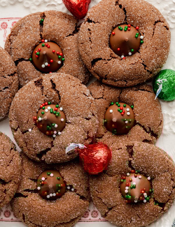Chocolate peanut butter blossoms on white cookie tray with red and green wrapped hershey's kisses.