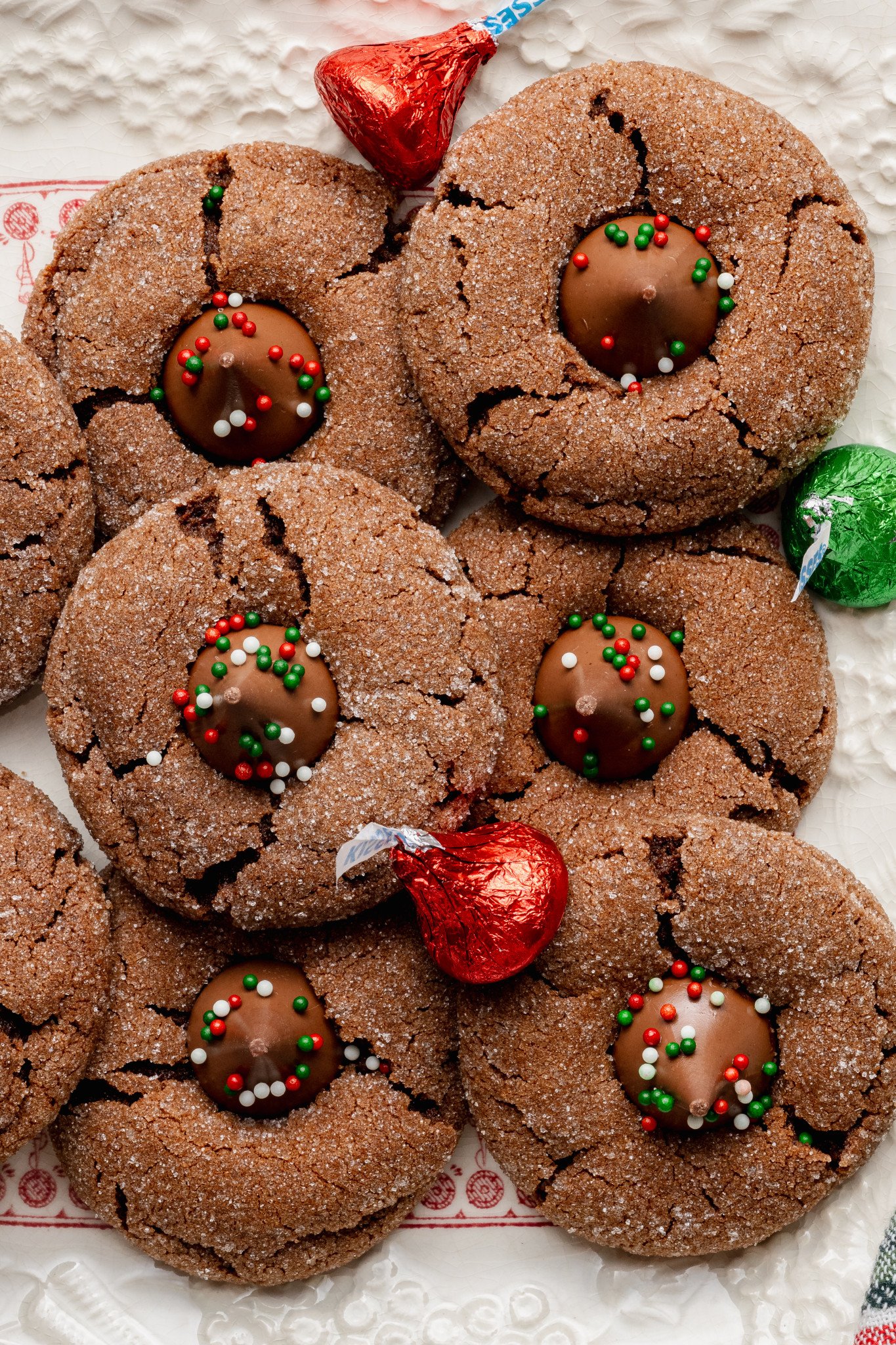 Chocolate peanut butter blossoms on white cookie tray with red and green wrapped hershey's kisses.