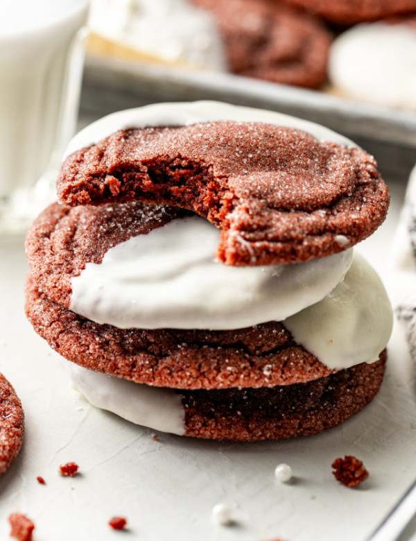 Four white chocolate red velvet cookies stacked on top of each other with a bite taken out of the top cookie.