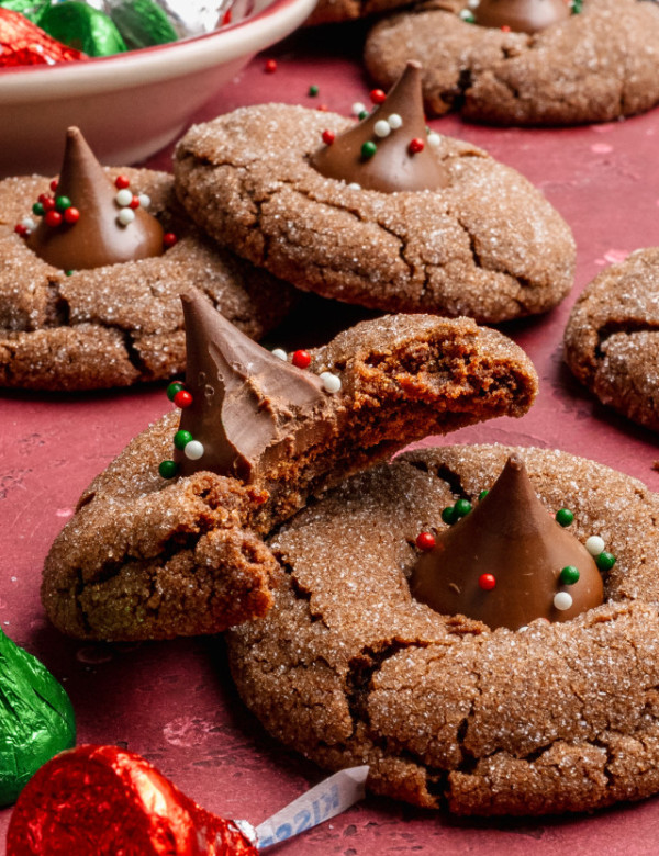 Chocolate peanut butter blossoms on table with one cookie having a bite taken out of the middle to show soft, fudgy center.