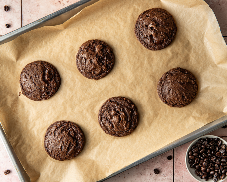 Six baked espresso martini cookies on parchment lined baking tray before being dipped in white chocolate.