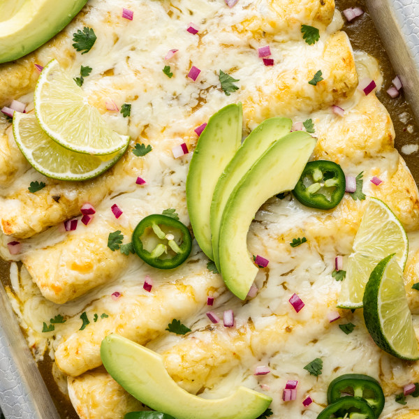 Green chicken enchiladas in baking pan topped with enchilada toppings.