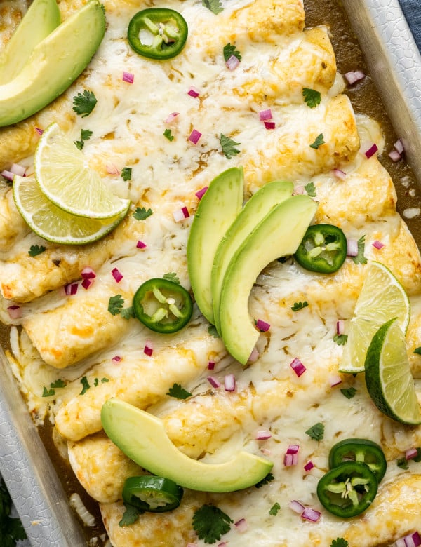 Green chicken enchiladas in baking pan topped with enchilada toppings.