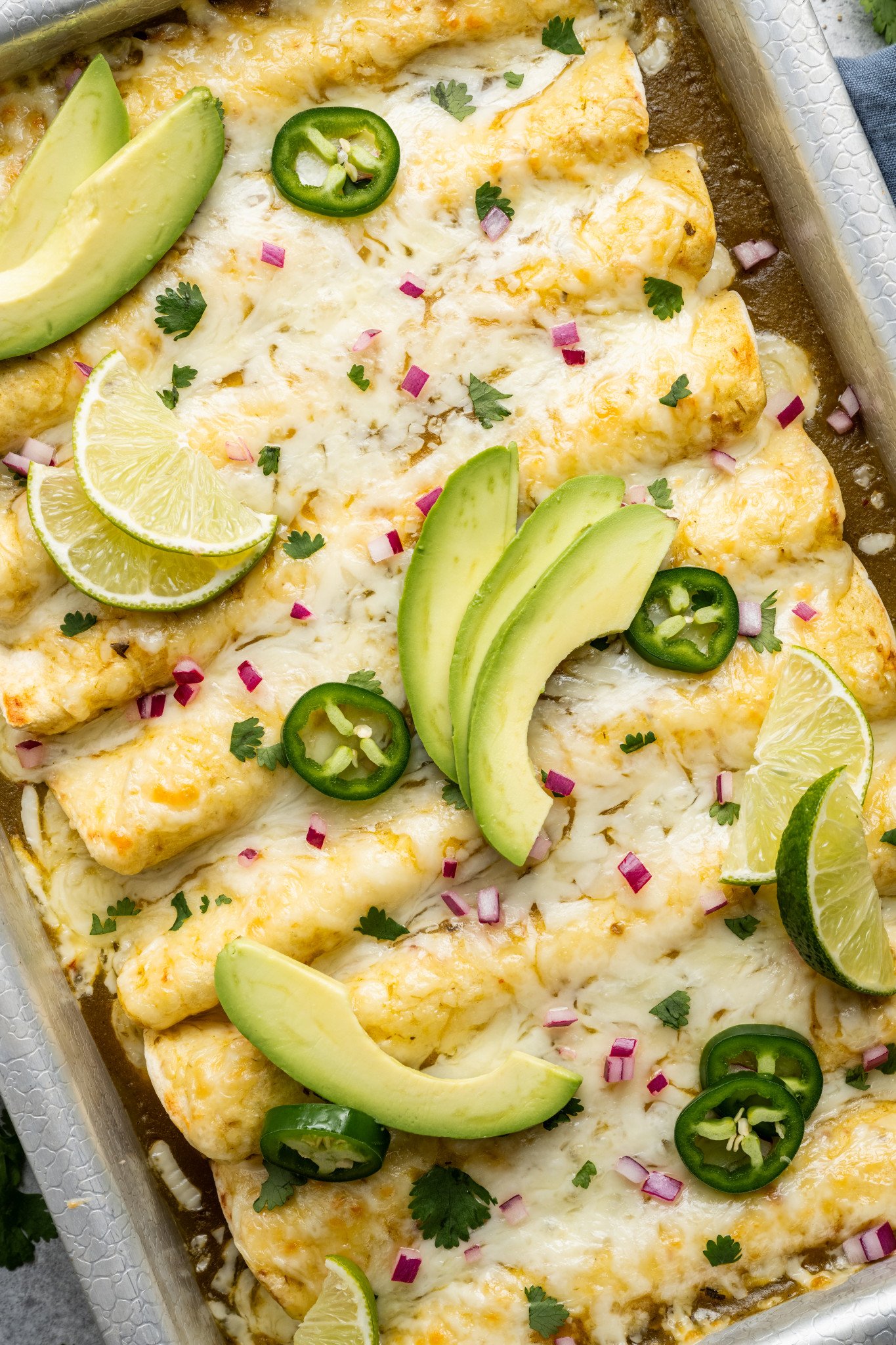Green chicken enchiladas in baking pan topped with enchilada toppings.