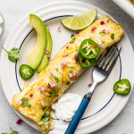 Green chicken enchilada on plate with toppings and a fork.