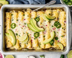 Green chicken enchiladas garnished with avocado, red onion, jalapenos, and lime wedges.