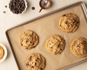 Six peanut butter dark chocolate chip cookies baked on parchment-lined baking tray.
