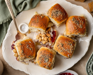 Six thanksgiving sliders on white serving plate with the top off one of the sliders so you can see the inside layers.