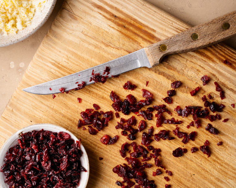 Chopping the dried cranberries on a cutting board with a sharp knife.