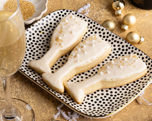 Three champagne sugar cookies on black and white tray with glass of champagne.