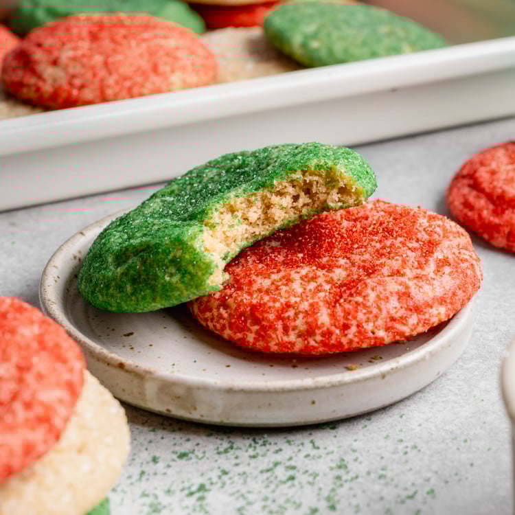 A red and green Christmas snickerdoodle on a small plate with a bite taken out of the top green cookie.