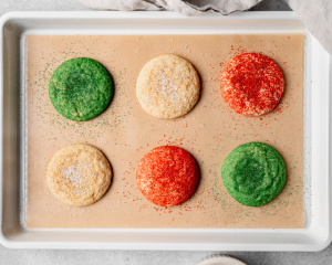 Six Christmas snickerdoodles baked on a parchment lined baking tray and sprinkled with extra sugar.
