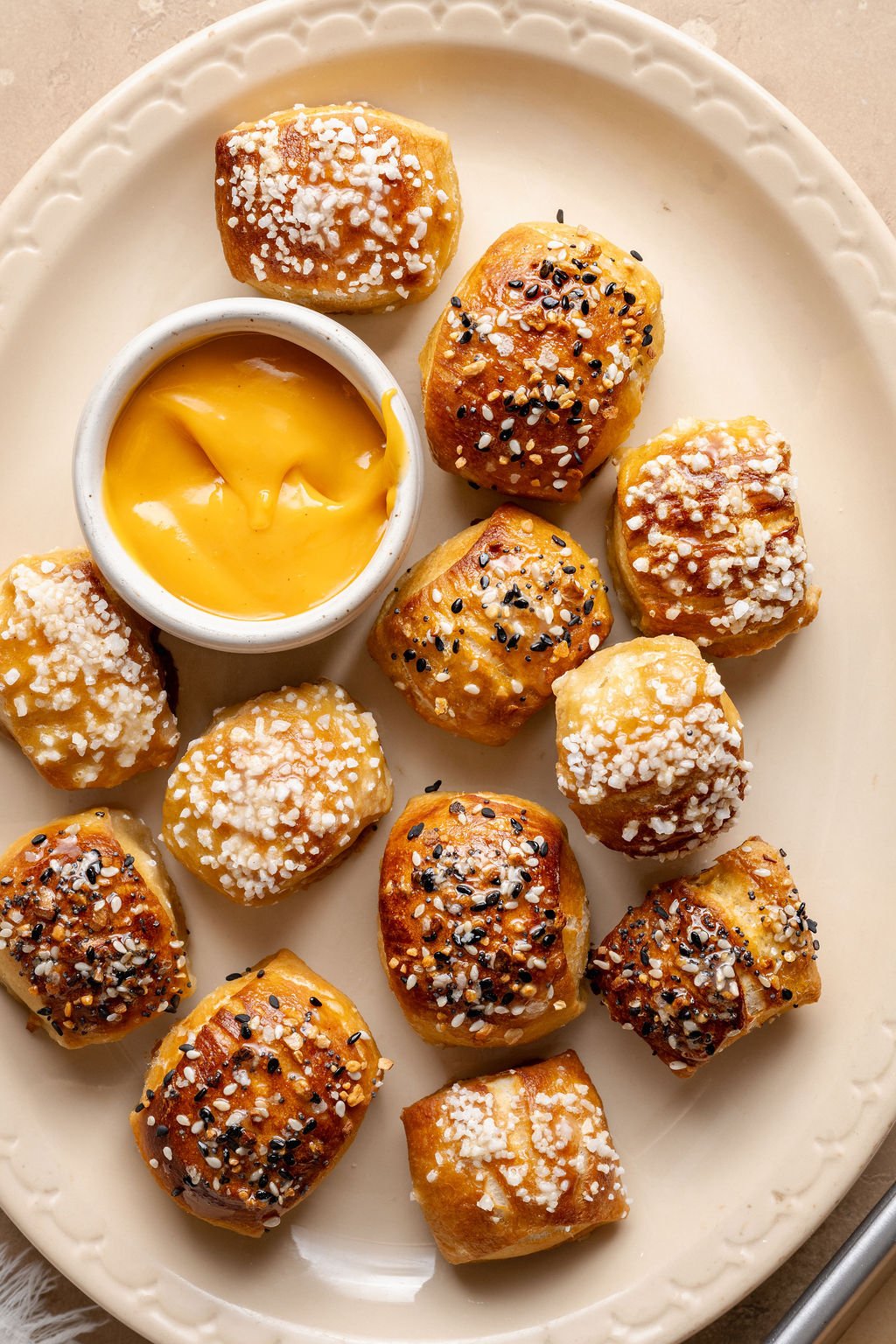 Overhead view of pretzel bites served on a cream-colored plate with a bowl of warm cheese sauce for dipping.