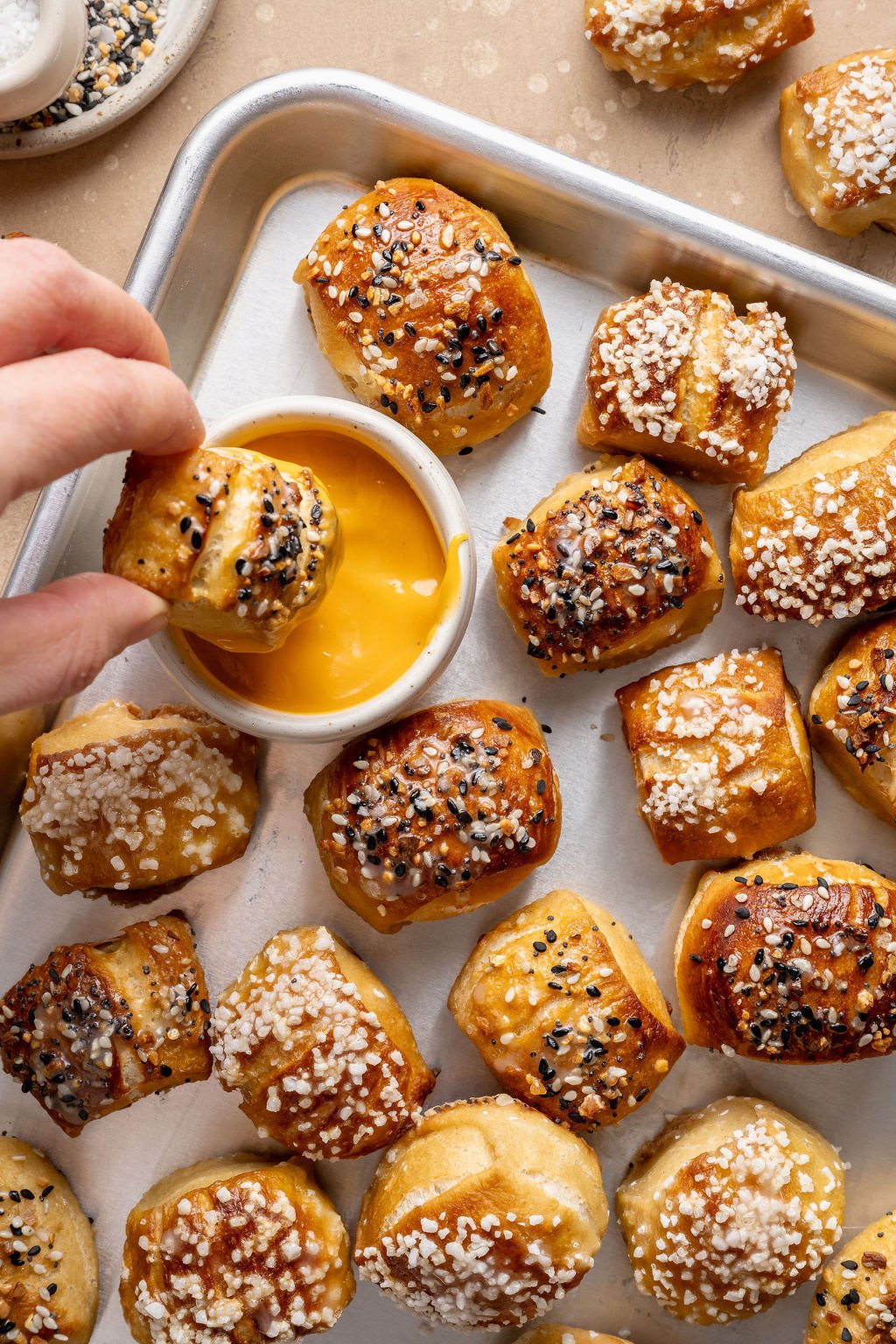 Overhead view of a hand dipping a warm pretzel bite topped with everything bagel seasoning into a bowl of cheese sauce.