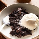 Gooey brownie pudding in a bowl with ice cream and spoon.