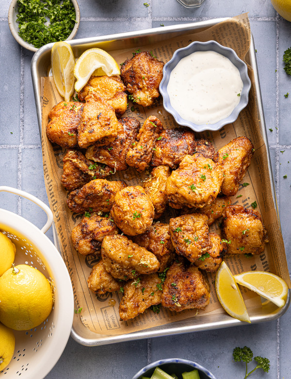 Lemon pepper boneless chicken wings cooked and placed on parchment-lined baking sheet garnished with fresh parsley and lemon wedges.