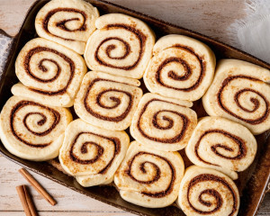 Overhead view of soft cinnamon rolls after their final rise, filling the baking dish with plump rolls and defined cinnamon spirals.