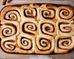 Overhead view of freshly baked cinnamon rolls in a baking dish, golden brown with soft centers and visible cinnamon swirls.