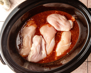 Adding the chicken breasts to the sauce in the crockpot.