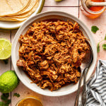 Slow cooker honey chipotle chicken in bowl with serving spoons on the side.