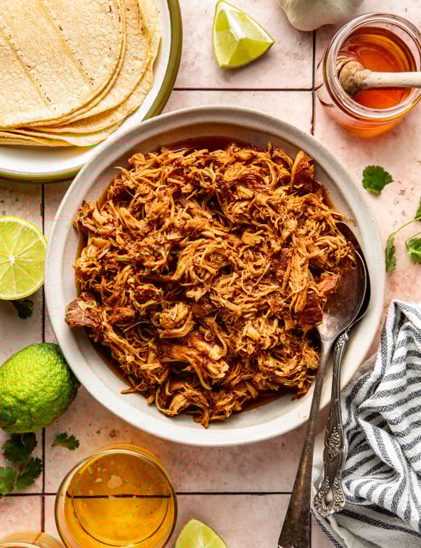 Slow cooker honey chipotle chicken in bowl with serving spoons on the side.