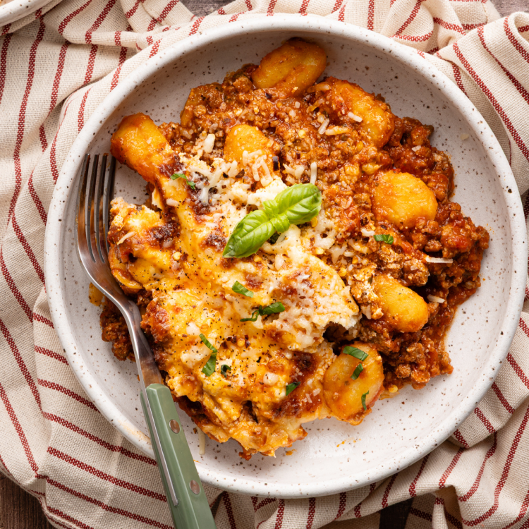 One-pan gnocchi lasagna in a small bowl for serving with a fork on the left side and garnished with fresh basil on top.