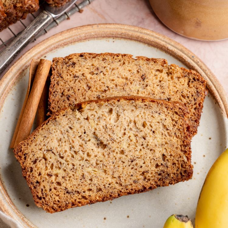 Two slices of banana bread on plate with cinnamon stick.