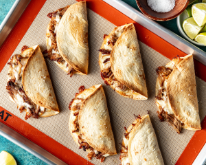 Six pork carnitas tacos baked on baking tray with silicone mat underneath.