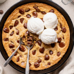 Chocolate chip cookie skillet topped with three scoops of vanilla ice cream and two spoons digging into the center.