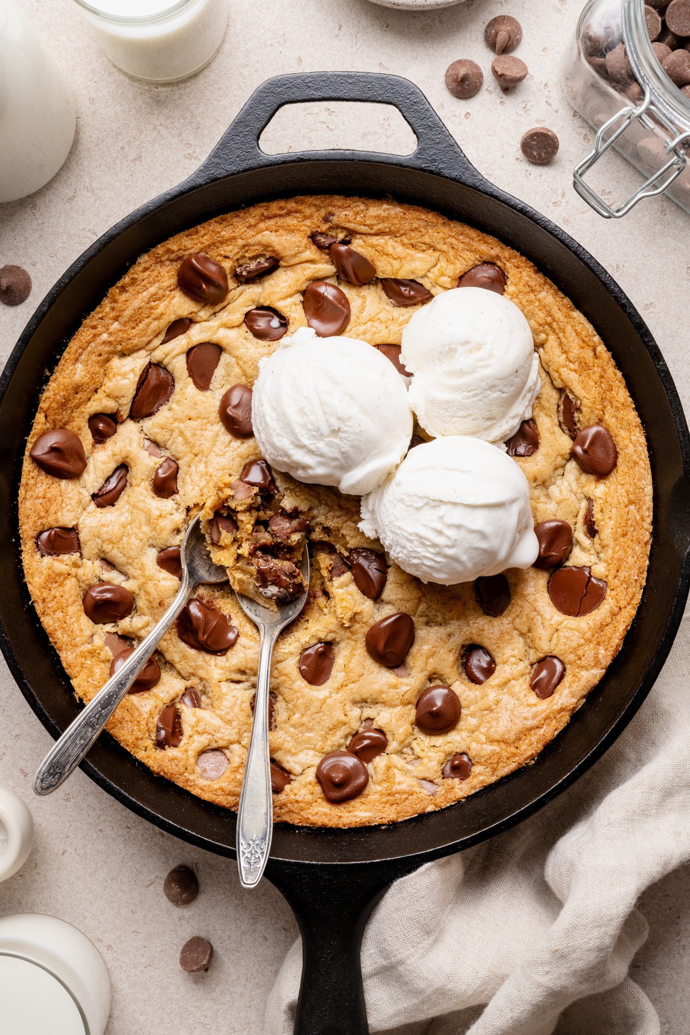 Chocolate chip cookie skillet topped with three scoops of vanilla ice cream and two spoons digging into the center.