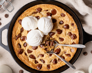 Cast iron skillet cookie topped with vanilla ice cream with two spoons digging into the center.