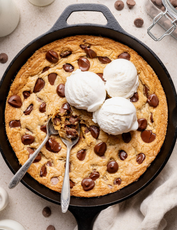 Chocolate chip cookie skillet topped with three scoops of vanilla ice cream and two spoons digging into the center.