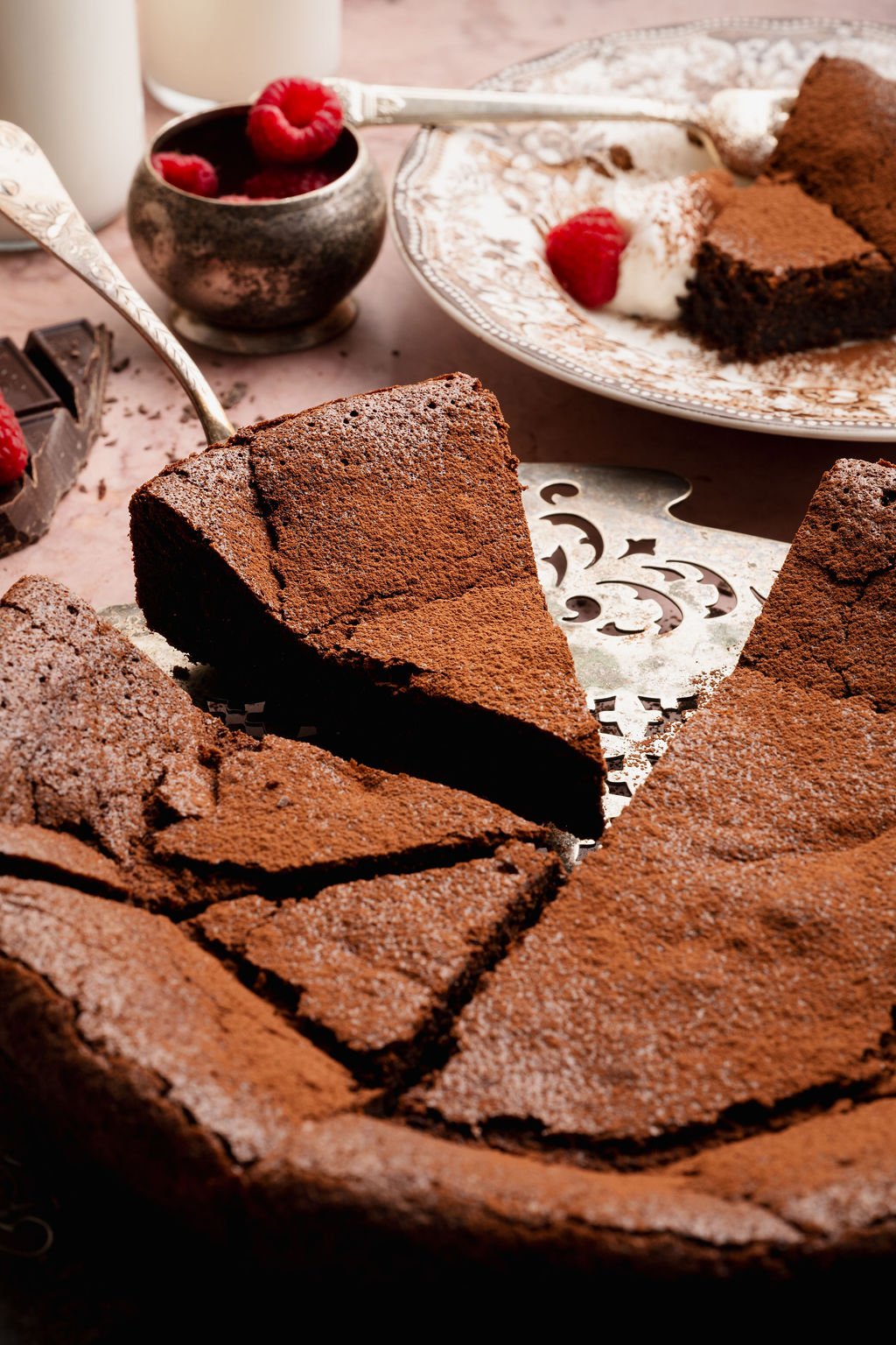 Close-up of several slices of flourless chocolate cake arranged on a vintage cake stand, dusted with cocoa powder and partially sliced.