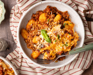 Bowl of gnocchi lasagna with fork on the side and garnish of fresh basil on top.