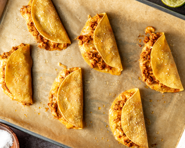 Six ground chicken tacos baked on parchment-lined baking tray.