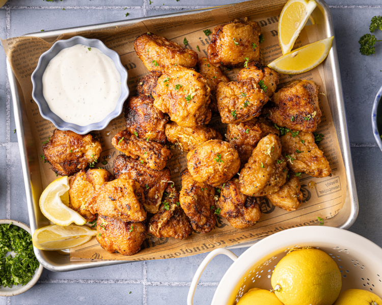Lemon pepper boneless wings cooked and garnished with fresh parsley and lemon wedges on parchment-lined baking tray.