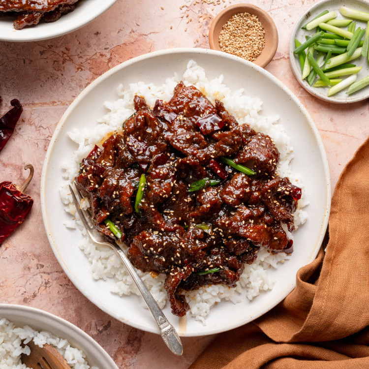 Mongolian beef served over rice on plate with fork on the side.