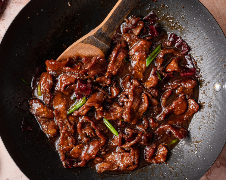 Cooked mongolian beef stirred in sauce in wok pan.