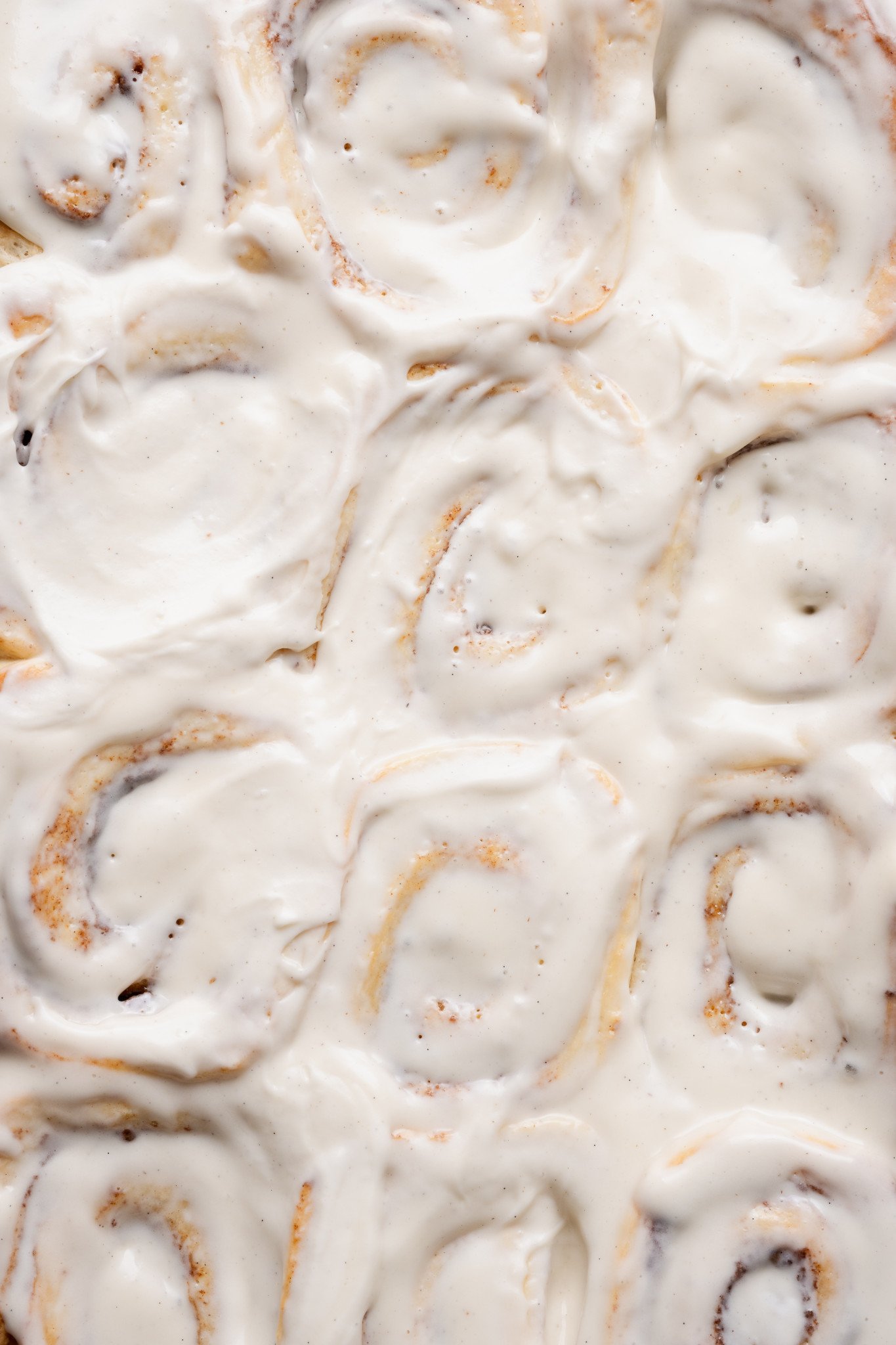 Tight overhead close-up of cinnamon rolls covered in thick cream cheese frosting, showing soft swirls and gooey centers.