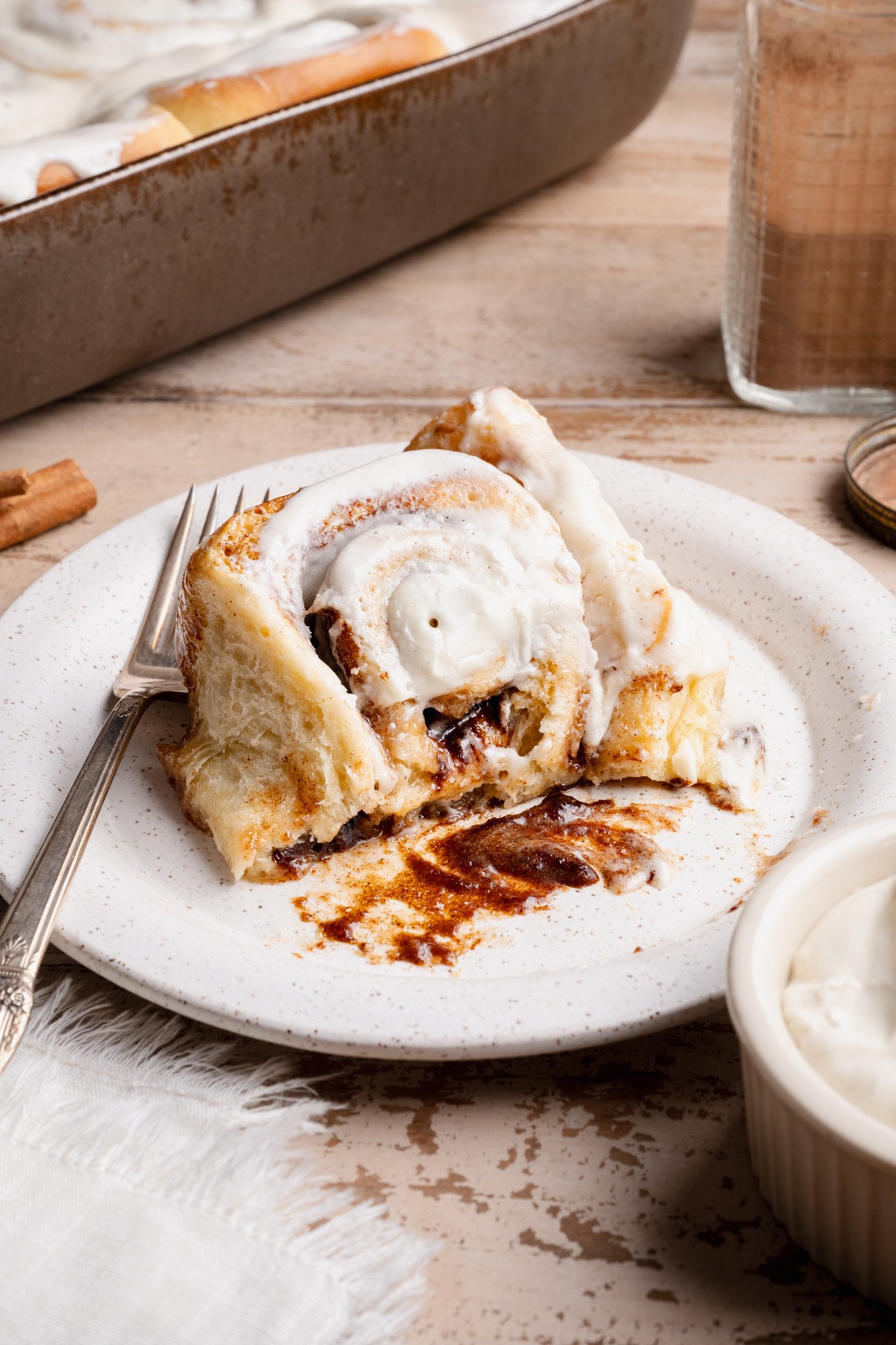 Close-up of a cinnamon roll pulled apart on a plate, showing a soft, fluffy interior and gooey cinnamon filling with cream cheese frosting.
