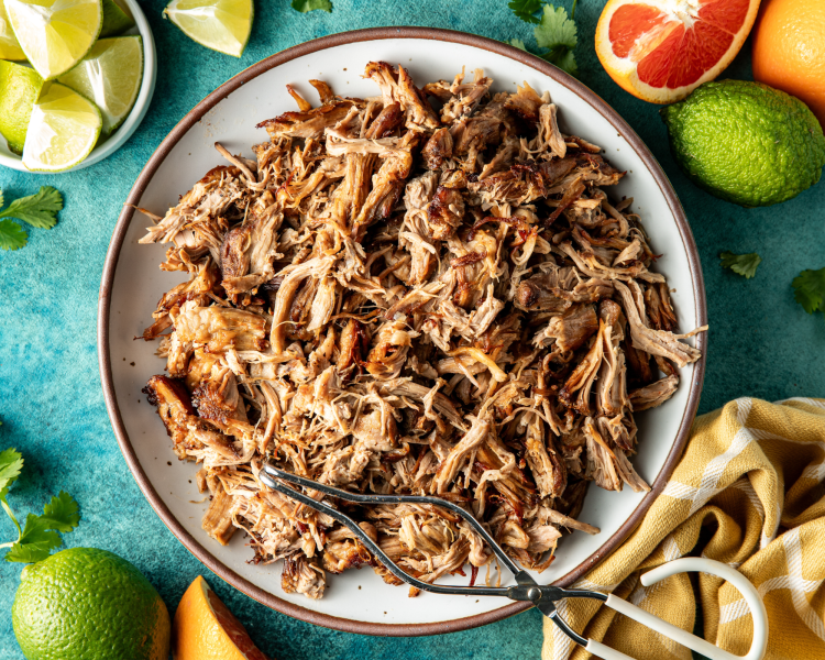 Pork carnitas finished and placed on serving dish with metal tongs for serving.