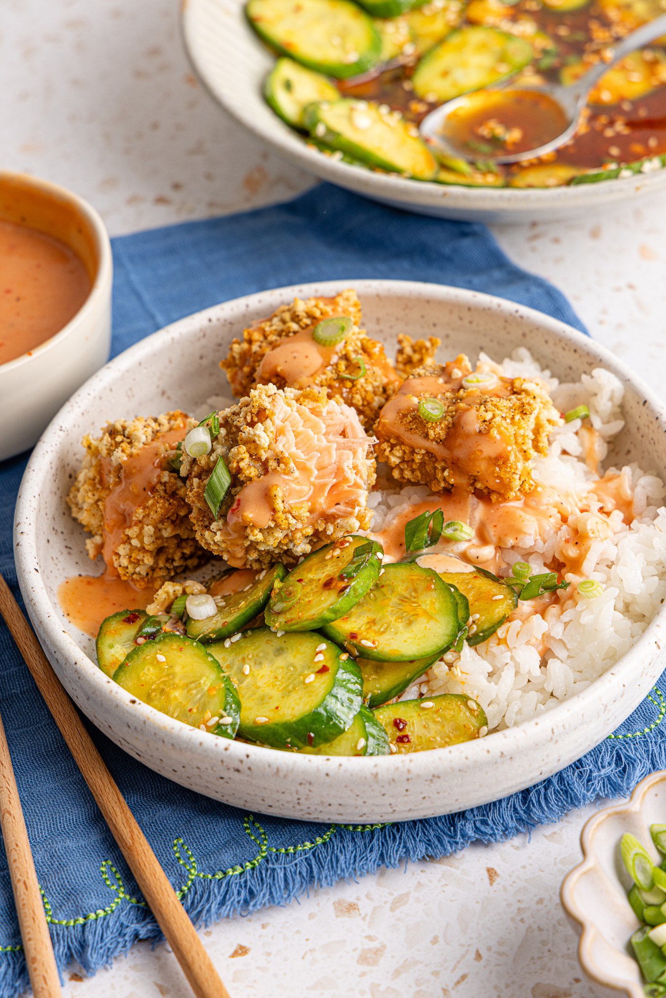 Salmon nuggets served in a bowl with rice and cucumber salad and drizzled with bang bang sauce. - 2