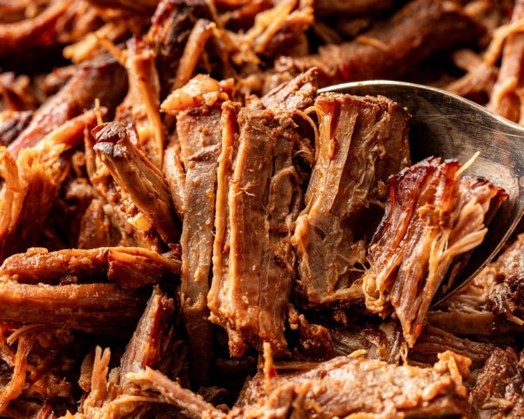 Close-up of shredded birria beef with a spoon lifting tender strands, highlighting the juicy texture and rich reddish-brown color.