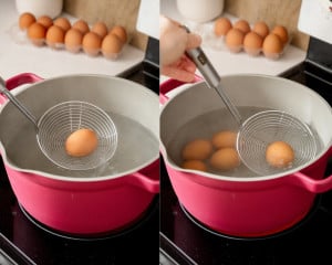 First image shows a brown egg being carefully lowered into boiling water using a stainless steel spider strainer. Second image shows multiple eggs gently placed into the pot with the strainer, fully submerged in hot water.