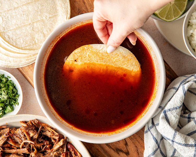 Dipping a white corn tortilla into warm consom&eacute; before adding it to the hot skillet.