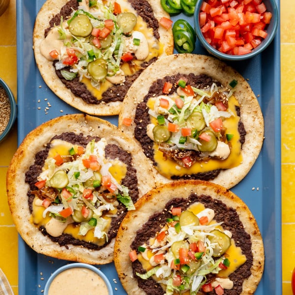 Four cheeseburger tacos with toppings added on blue food tray with burger sauce in a small bowl on the side.