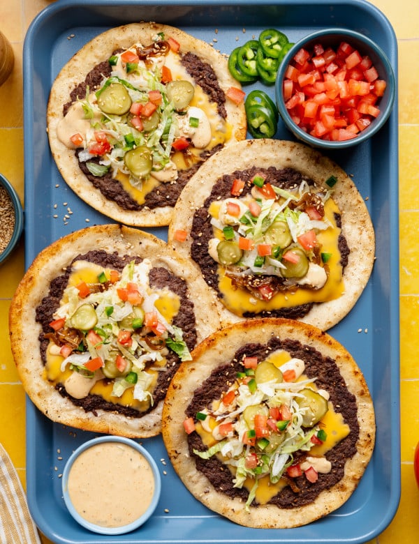 Four cheeseburger tacos with toppings added on blue food tray with burger sauce in a small bowl on the side.