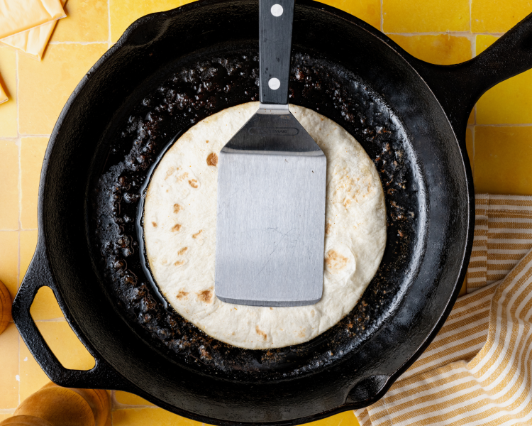 Pressing the tortilla and burger down on a cast-iron skillet to cook the beef.