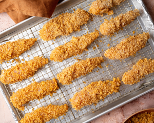Twelve chicken tenders breaded and placed on prepared baking sheet.